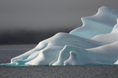 A deeply sculpted iceberg floats in the open waters of Scoresbysund Fiord with black clouds behind. East Greenland. 2005