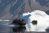 Tourist zodiacs cruise amongst icebergs in Fhn Fiord, backed by the 2100m peaks of Milne Land. East Greenland. 2005