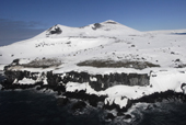 Snow filled crater and penguin colony. Basalt columns in foreground. Antarctica.