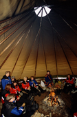 Tourists sit round a fire in a lavvu and learn about the Sami culture. Jukkasjarvi. Sweden. 2003