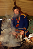 Sami youth sits by a fire in a sami lavvu, he is cooking reindeer meat. Jukkasjarvi. Sweden. 2003