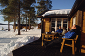 Visitors relax in the sun outside a cabin at a wilderness camp near Jukkasjarvi. Sweden. 2003