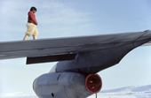Inuit boy in polar bear pants climbs on wing of American plane. Northwest Greenland. 1980