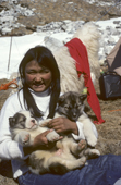 Inuit girl plays with husky puppies outside her tent at a hunting camp in spring. Moriussaq. NW Greenland. 1980