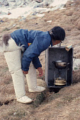 Birgethe,an Inuit woman. tends a Primus stove, at Spring hunting camp near Cape Atholl. She is wearing traditional seal skin Kamik (boots). Northwest Greenland. (1980)