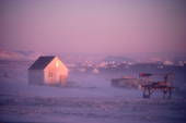 Sunlight catches a house in an autumn storm with wind driven snow in Moriussaq. Northwest Greenland. 1987