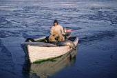 Jens, an Inuit hunter, returns to the village of Moriussaq with a seal over the side of his boat after an autumn day's hunting. Moriussaq. Northwest Greenland. (1987)