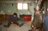 Inuit hunter, Ituko, works on his hunting equipment during the polar night. On the right a walrus carcass hangs up. Northwest Greenland. 1987