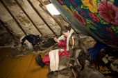 Mira Khudi, a Nenets woman, sewing a pair of boots in her reindeer skin tent at winter pastures. Yamal, NW Siberia, Russia