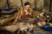 Inside her family's tent, Nyaneynya Serotetto, a Nenets woman, threads a needle with sinew while making a reindeer skin 'Malitsa' (traditional tunic) for her son. Yamal, NW Siberia, Russia.