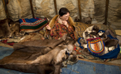 Inside her family's tent, Nyaneynya Serotetto, a Nenets woman, smooths a length of sinew while sewing a reindeer skin 'Malitsa' (traditional tunic) for her son. Yamal, NW Siberia, Russia.