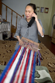 Vayla Khudi, takes a call on her mobile phone while weaving a woollen Nenets man's belt on a traditional hand loom. Yar-Sale, Yamal, NW Siberia, Russia.