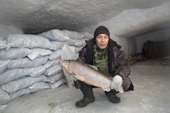 Velodia Yando, a Nenets fisherman, holds an 17.5 lb Broad Whitefish (Coregonus nasus) inside an ice house by the Yuribey River. The ice house is used to freeze and store fish. It was built into the permafrost, 20 feet under the surface of the tundra and covers an area of 900 square metres. Gydan Peninsula, Yamal, Siberia, Russia
