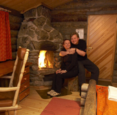 A loving couple sit by the fire in a log cabin. Hotel Kakslauttanen, Kakslauttanen, Lapland, Finland. MR